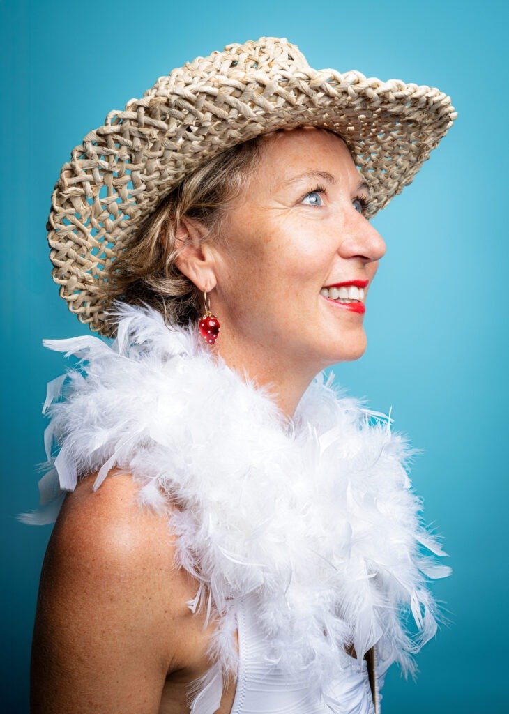 Portrait de femme en studio sur fond bleu, chapeau de paille et boa blanc