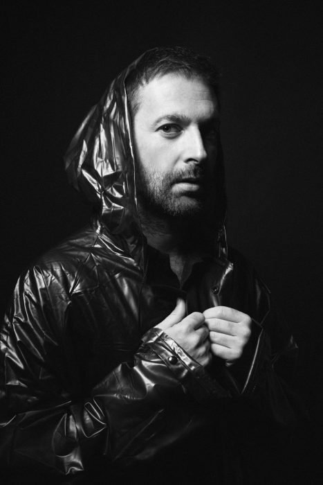 Portrait d’homme barbu en noir et blanc, capuche brillante et regard intense sur fond sombre